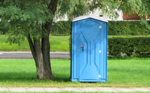 deluxe porta potty under a tree next to a pathway